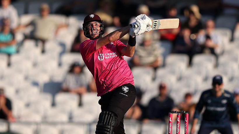 Somerset all-rounder Craig Overton in action, hitting a ball into the distance in front of him on the leg-side.