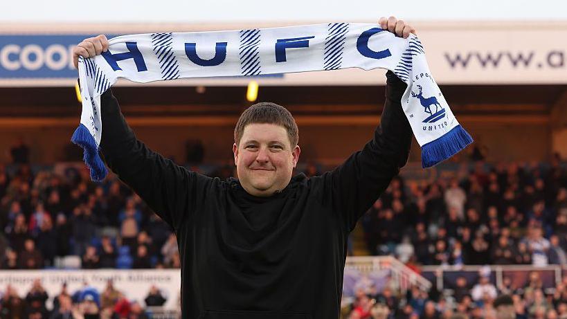 Hartlepool owner Landon Smith lifts a scarf above his head on the pitch ahead of the match against Altrincham.