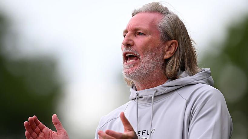 Robbie Savage in a grey hoodie claps his hands