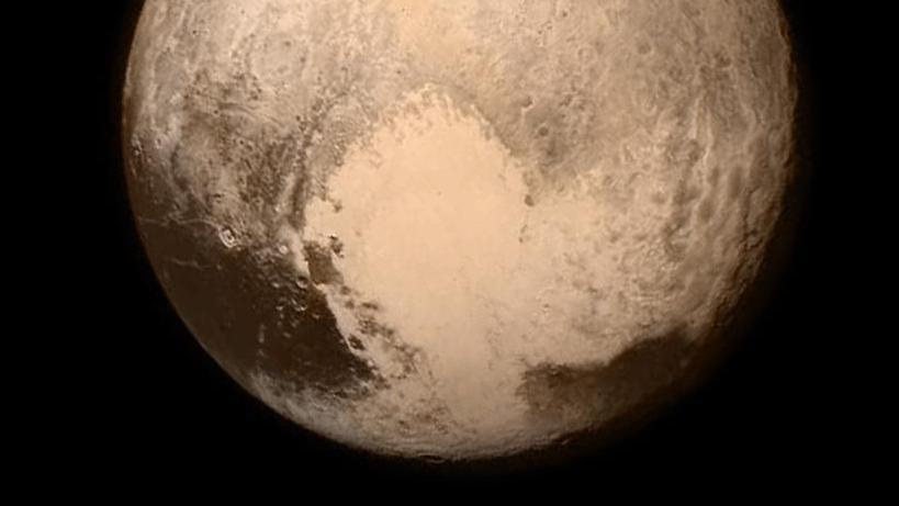 The planet Pluto appears as a sandy brown in the blackness of space with what appears to be a light coloured heart shape appearing in the southern hemisphere