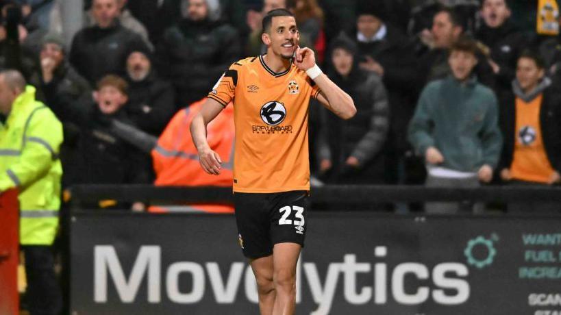 Gassan Ahadme holds his finger up to cup his ear in celebration after scoring for Cambridge United