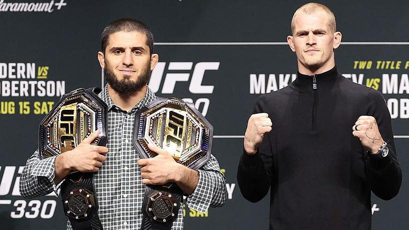 Islam Makhachev has the UFC lightweight and welterweight titles on his shoulder and stands next to Ian Machado Garry, who is holding up both his fists