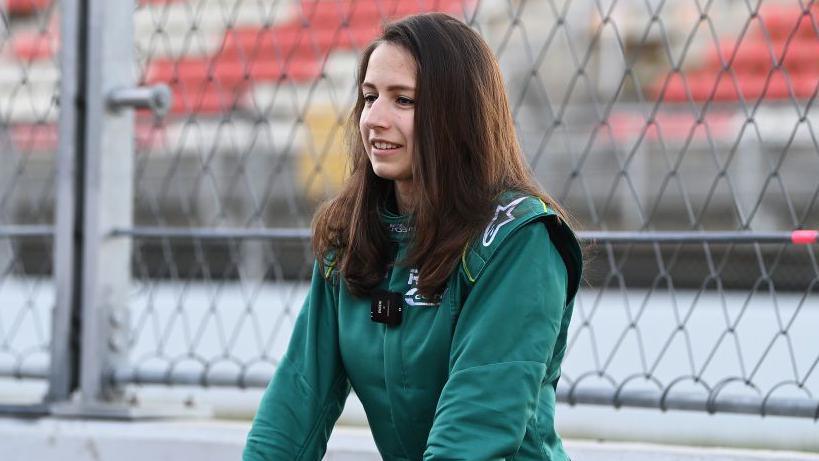 Megan Gilkes in a green race suit in front of a chain link fence