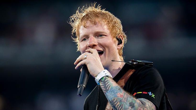 Ed Sheeran singing at a concert in Madrid. He is wearing a black T-shirt.
