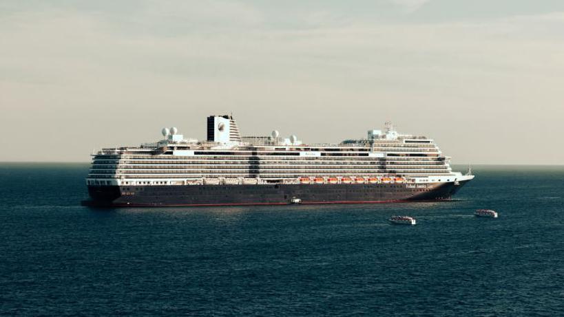 A large cruise ship on a sunny day with two tender vessels headed towards it.