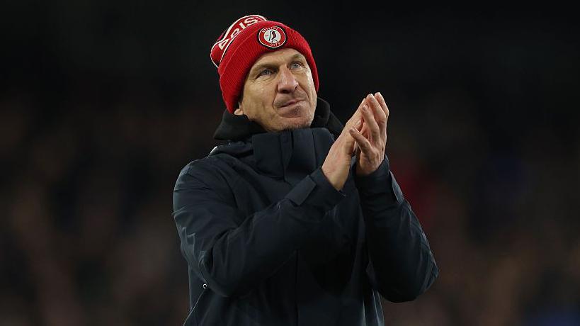Gerhard Struber wearing a Bristol City bobble hat and coat and clapping his hands while walking on the pitch at the end of the match with Ipswich