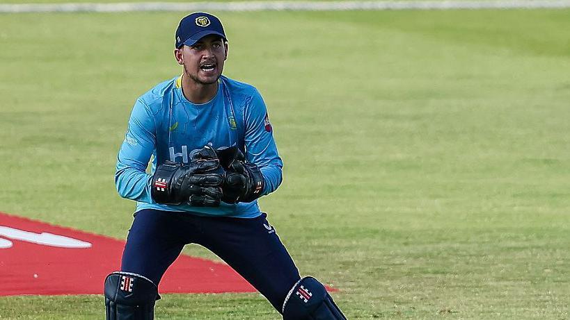 Kai Smith in action for Warwickshire in a T20 Blast game. He is wearing a light blue Bears top, navy trousers and wicket-keeper gloves and pads.