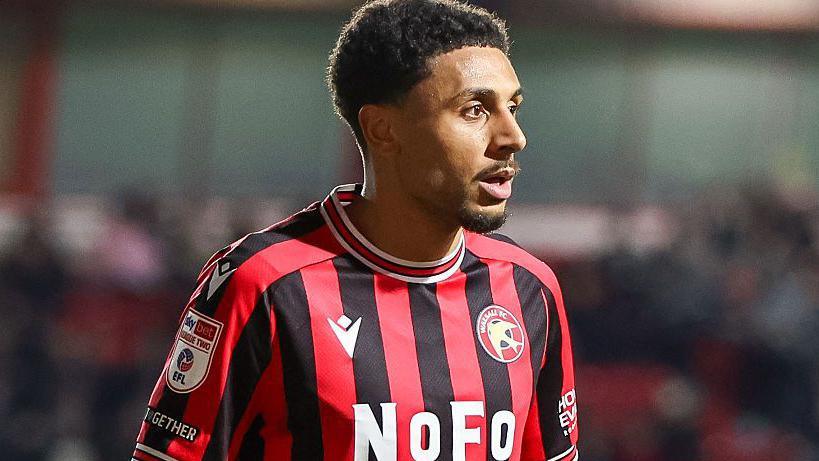 Brandon Comley looking to the right of frame in a red and black striped Walsall shirt