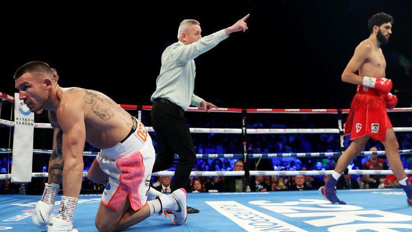A man on all fours in a boxing ring while the referee waves his opponent away.