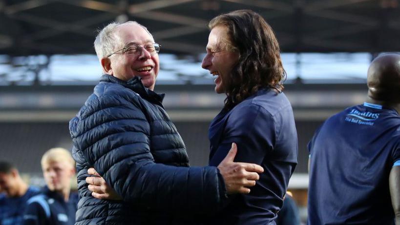 Rob Couhig, wearing a blue coat, and Ainsworth, wearing a blue shirt, embrace after Wycombe beat MK Dons in the League One play-off semi-finals in 2022