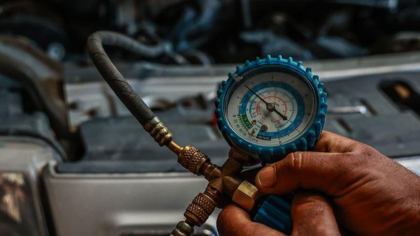 A pressure gauge is used to check the refrigerant levels in a car's air conditioning