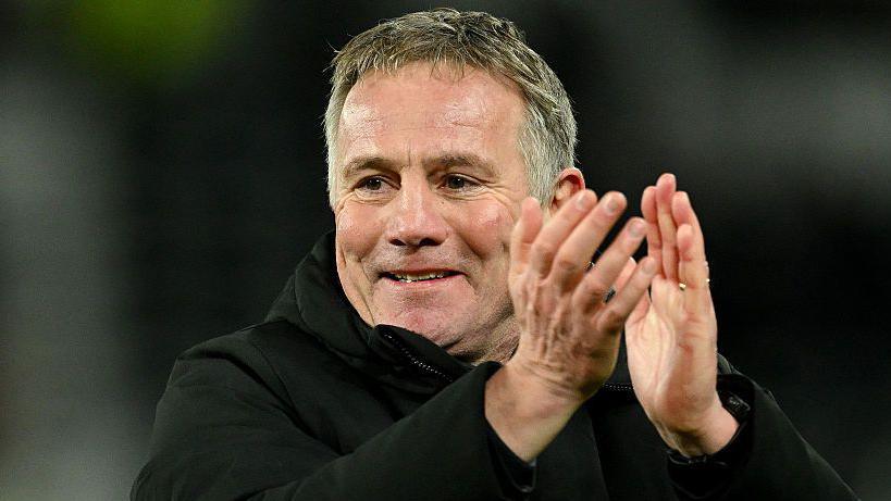 Phil Parkinson smiles and applauds wearing a black coat