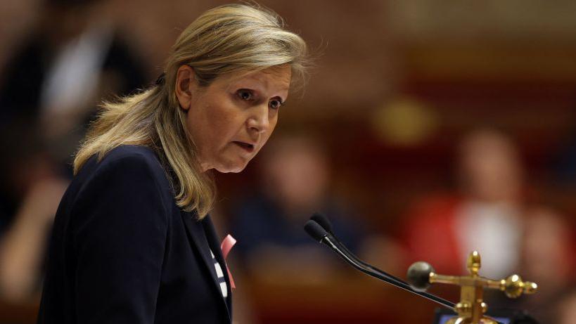 A woman with blonde hair and a black jacket talks into a microphone