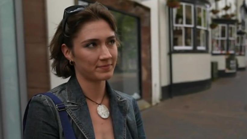 Student Aislinn Humphries, wearing a denim jacket and a large necklace, standing on a street