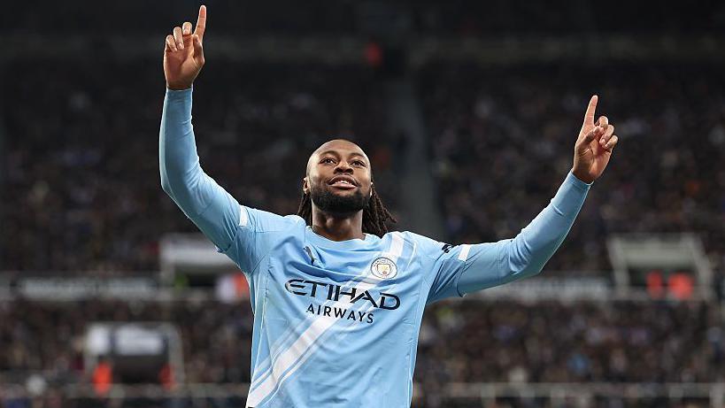 Antoine Semenyo celebrates scoring for Manchester City with an arms-raised salute as he wears a long-sleeved predominantly light blue City home shirt