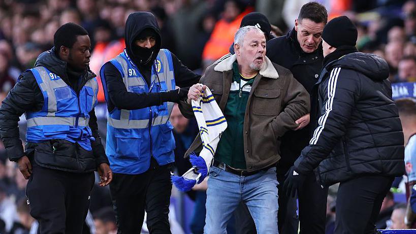 A Leeds fan is escorted from the pitch on Sunday after attempting to confront Daniel Farke