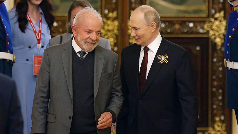 Brazil's President Luiz Inácio Lula da Silva and Vladimir Putin walk through a gold-encrusted palace in Moscow, smiling at one another