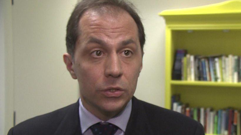 Andrea Cipriani is seen from the shoulders up and is wearing a black suit jacket with a purple and white tie. 