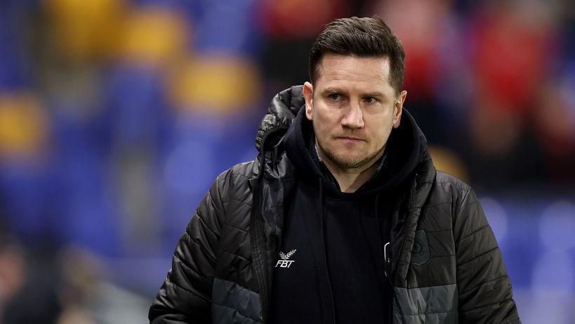 Lee Bell walks along the touchline after a game in his black Crewe puffer jacket