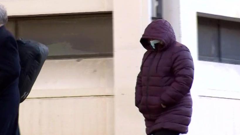 Rachel Limbrick is walking to court. She is wearing a purple jacket and is hiding her face behind a face mask.