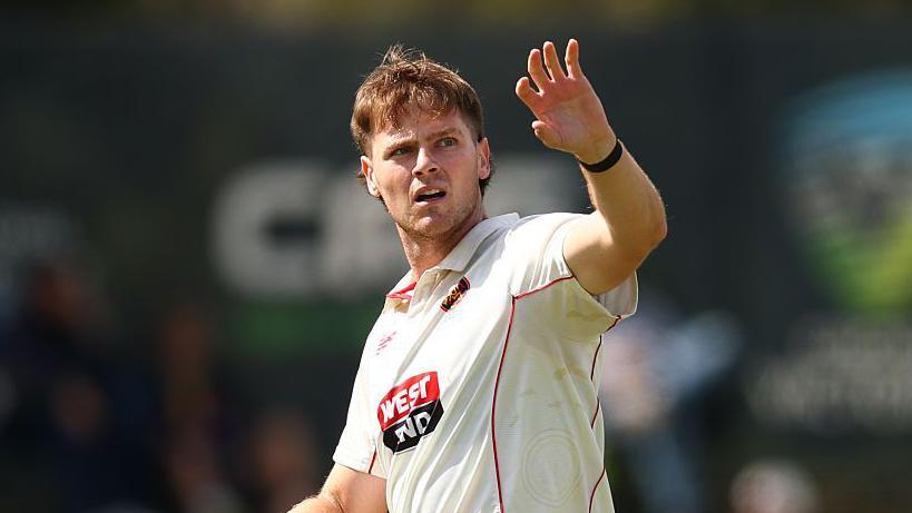 Liam Scott holding his left arm in the air to catch a ball that he is looking over his left shoulder towards. He is walking on the pitch during a match for Adelaide Strikers