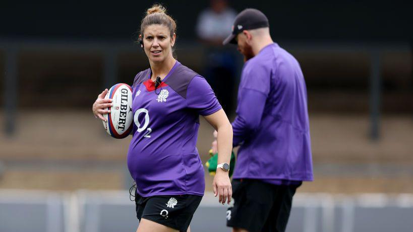 A pregnant Sarah Hunter holding a rugby ball in training