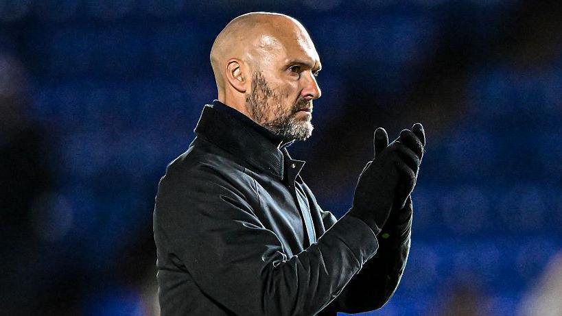 Peterborough United manager Luke Williams dressed all in black clapping his hands. 
