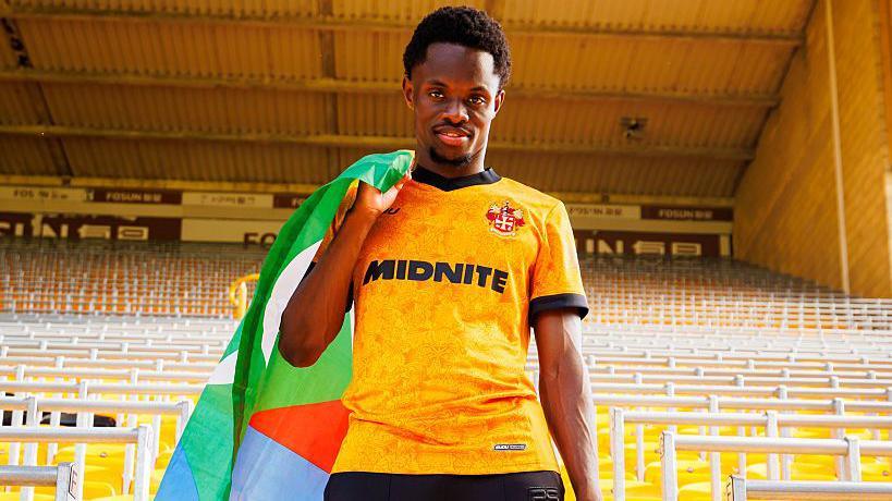 Rafiki Said wears the old gold Wolverhampton home shirt while in a stand at Molineux carrying a Comoros flag of green, blue and red over his shoulder