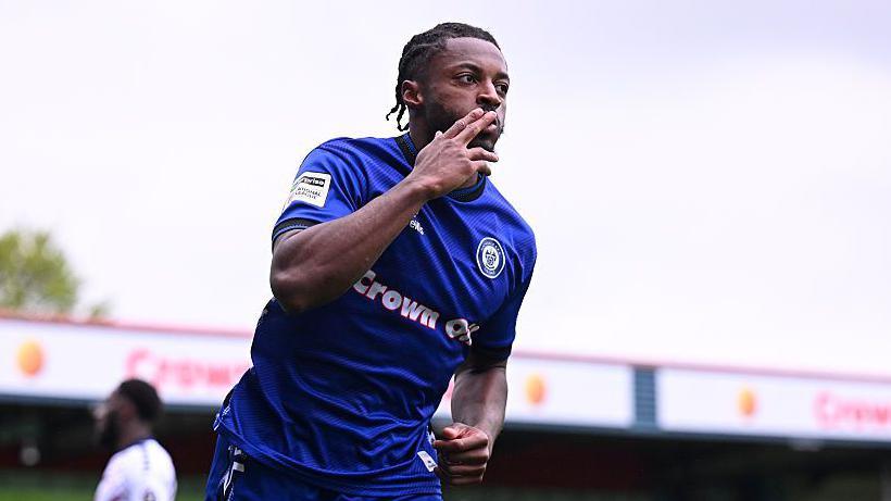 Rochdale's Devante Rodney celebrating scoring by kissing his index finger while wheeling away.