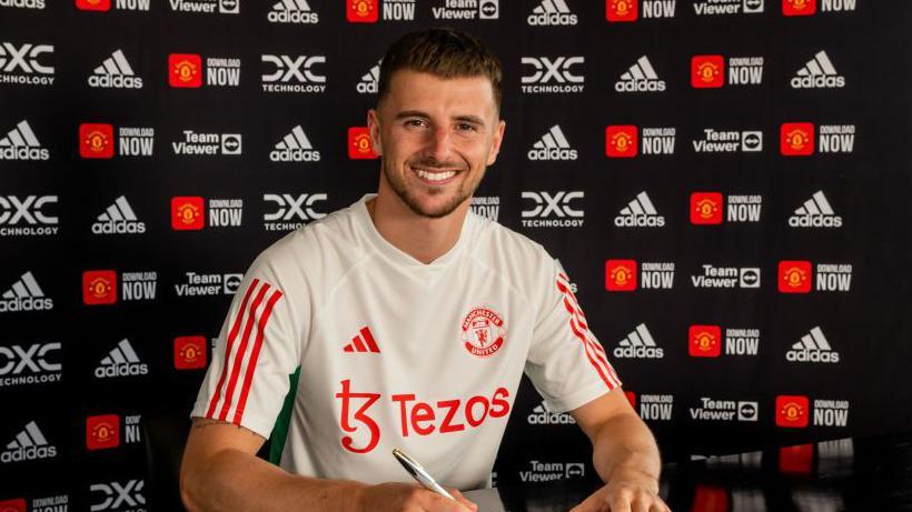 Mason Mount smiles towards the camera while signing his Manchester United contract.