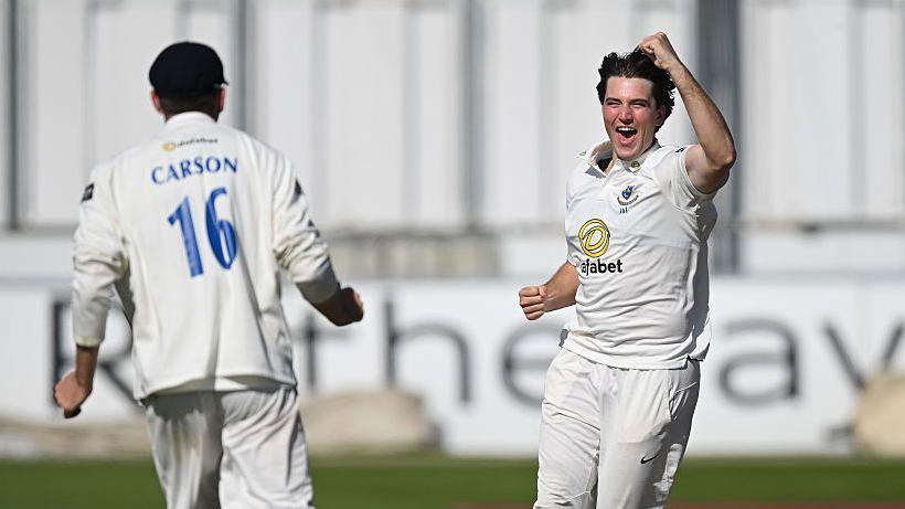 James Coles celebrating taking a wicket for Sussex in the County Championship by punching the air with his left hand next to team-mate Jack Carson.