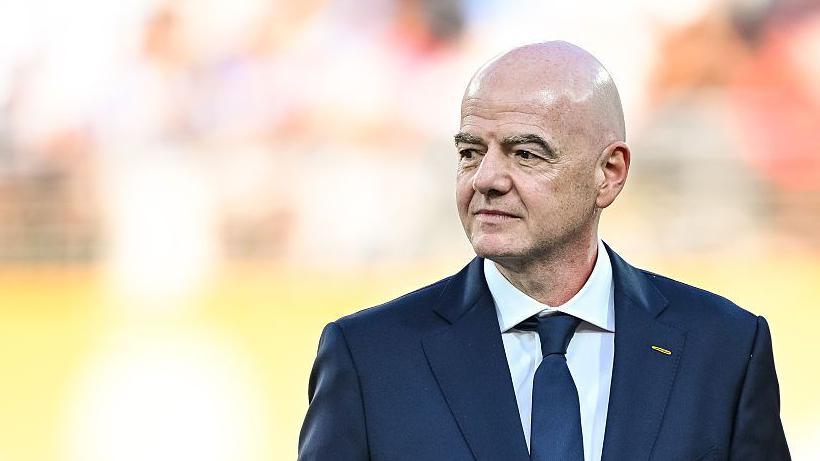 Gianni Infantino, wearing a dark suit and tie, looks to his right