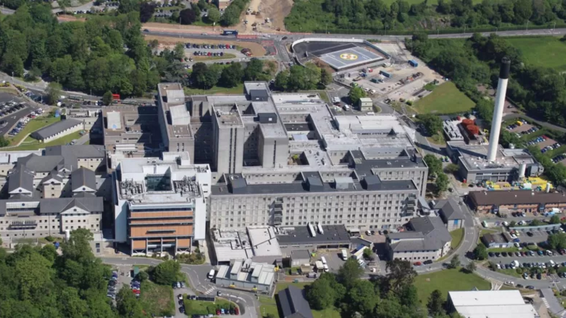 An aerial view of Derriford Hospital, with a helipad seen in the right hand corner surrounded by bits of trees and greenery