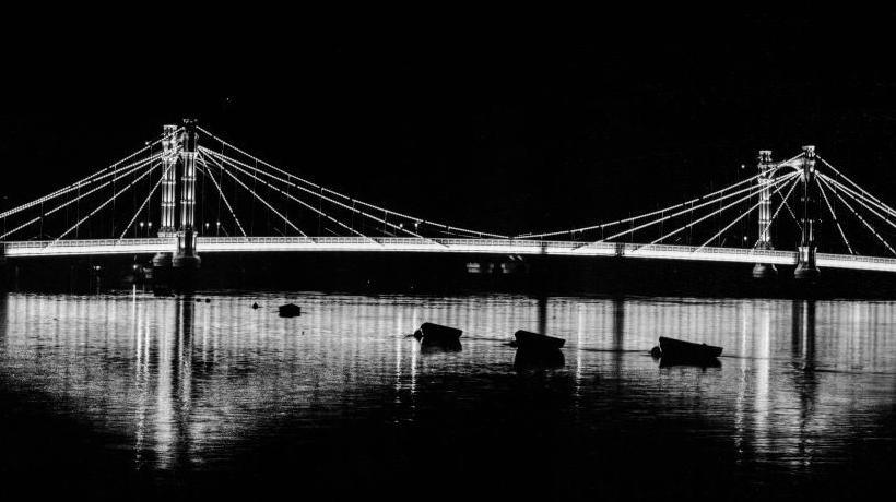 Albert Bridge, Kensington and Chelsea, Greater London Authority, 1960-1985. Albert Bridge illuminated at night, with small boats moored in the foreground