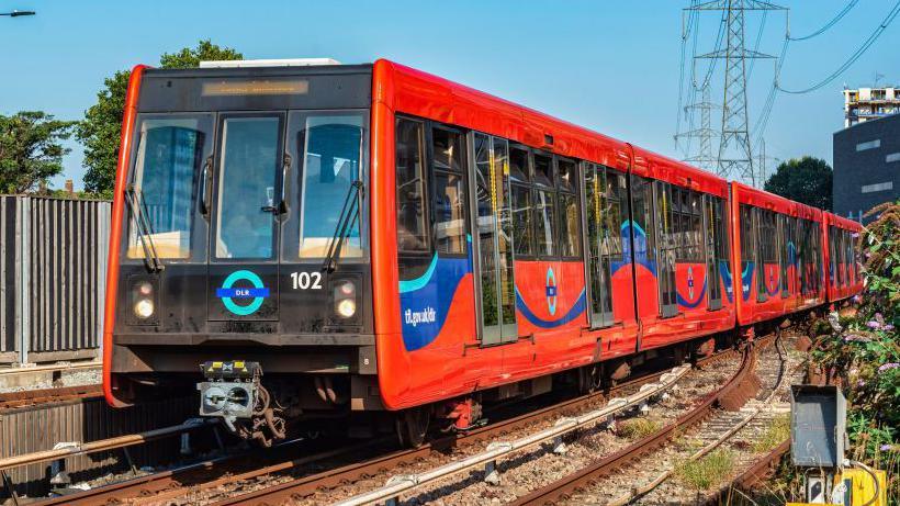 Red DLR train on rail tracks with electricity pylons in the background