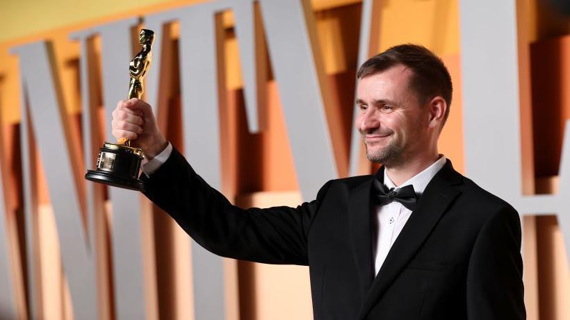 Rhys Salcombe attends the 2025 Vanity Fair Oscar Party wearing black tuxedo and holding up Oscar statuette smiling