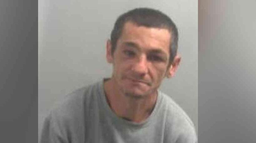 Custody photo of a man. He is wearing a grey jumper and looks disengaged.