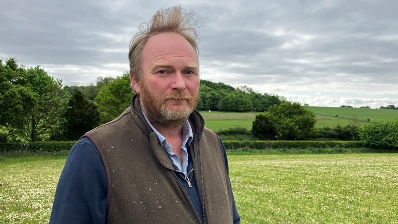 George Brown behind a landscape he is wearing a brown fleece vest which is behind a dark blue jumper.