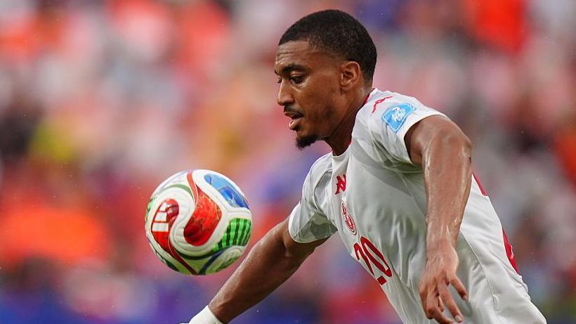 Yan Valery in white Tunisia playing kit and the number 20 in the middle of the shirt written in red controls a bouncing ball