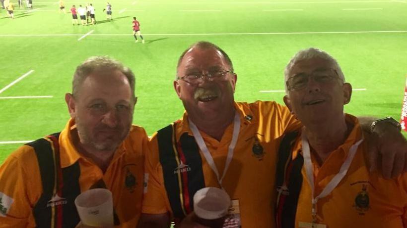 Rob Ewen stood with two other men with pints of beer in their hand. Rob is in the middle and smiling at the camera. 