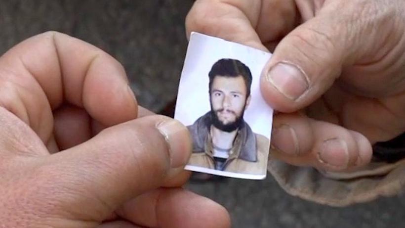 A photo the size of a photo from a photo-machine booth and in the dimensions of a passport ID photo being held by Dalaal's thumb and finger and being passed to the BBC's correspondent