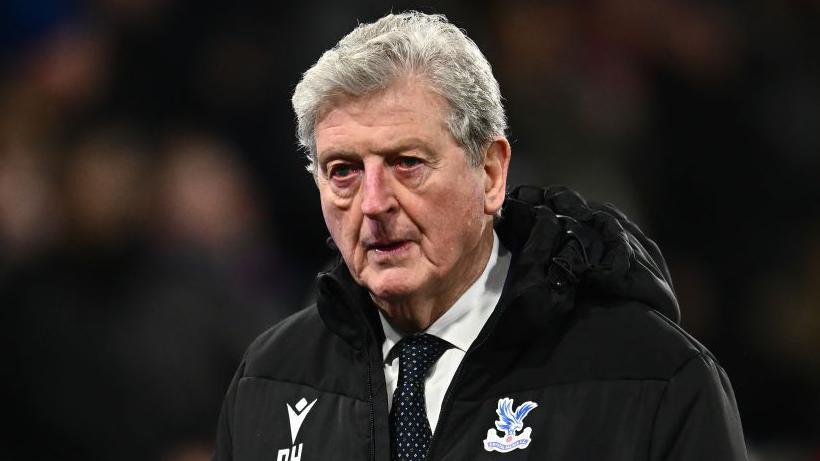 Roy Hodgson wearing a dark Crystal Palace coat with an eagle on it over a white shirt and spotted tie