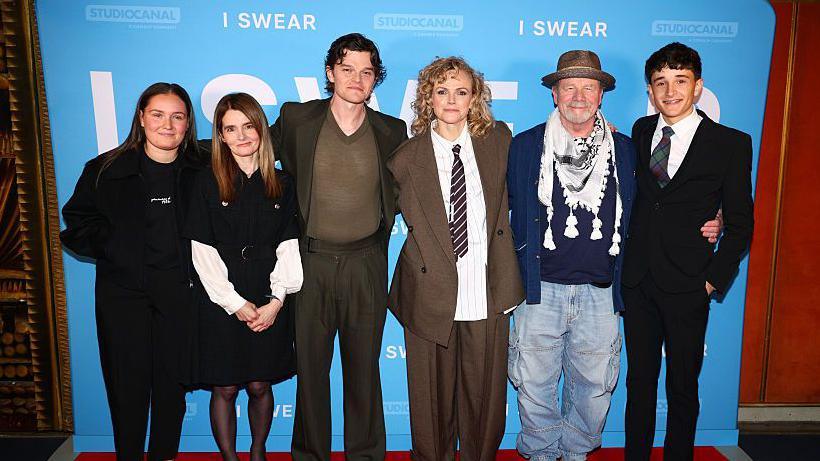 Andrea (far left), with the cast of I Swear - Shirley Henderson, Robert Aramayo, Maxine Peake, Peter Mullan and Scott Ellis Watson, standing on the red carpet, with the I Swear poster behind them.
