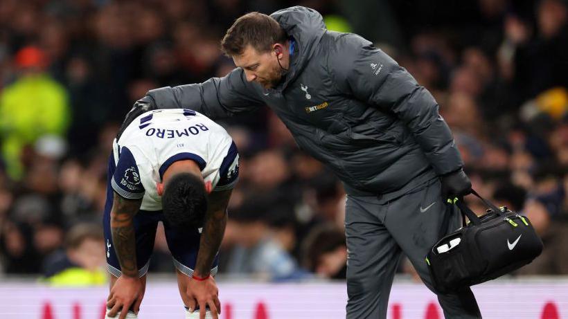 Tottenham defender Cristian Romero bends over in pain