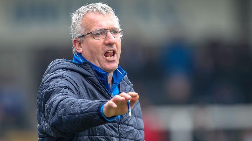 Tim Flowers points with a pen in his right hand and shouts instructions during a match