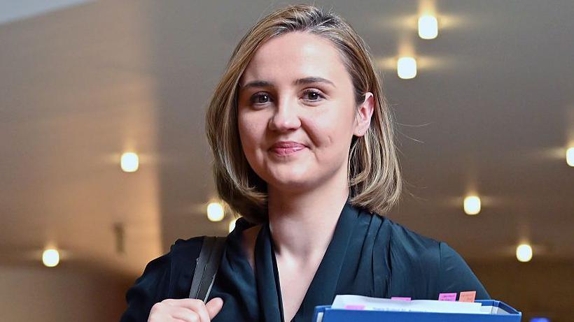 Housing Secretary Màiri McAllan wearing a dark top and carrying a bag over her shoulder and a blue folder in her other hand