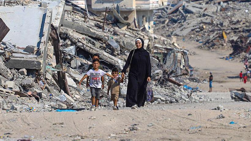 A Palestinian woman walks with children along a path lined with piles of rubble in the Sheikh Radwan neighbourhood of Gaza City