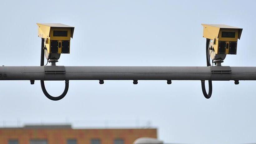 Two yellow speed cameras on the top if a horizontal metal bar over a road