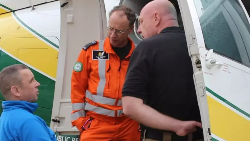 Rob Hope is sitting in a wheelchair talking to two paramedics next to the air ambulance 