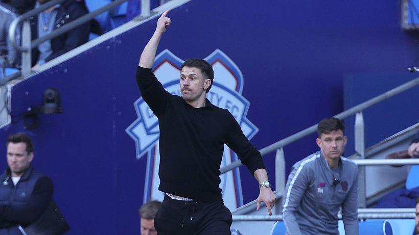 Aaron Ramsey all in black with arm raised on the touchline during his spell as Cardiff's interim boss